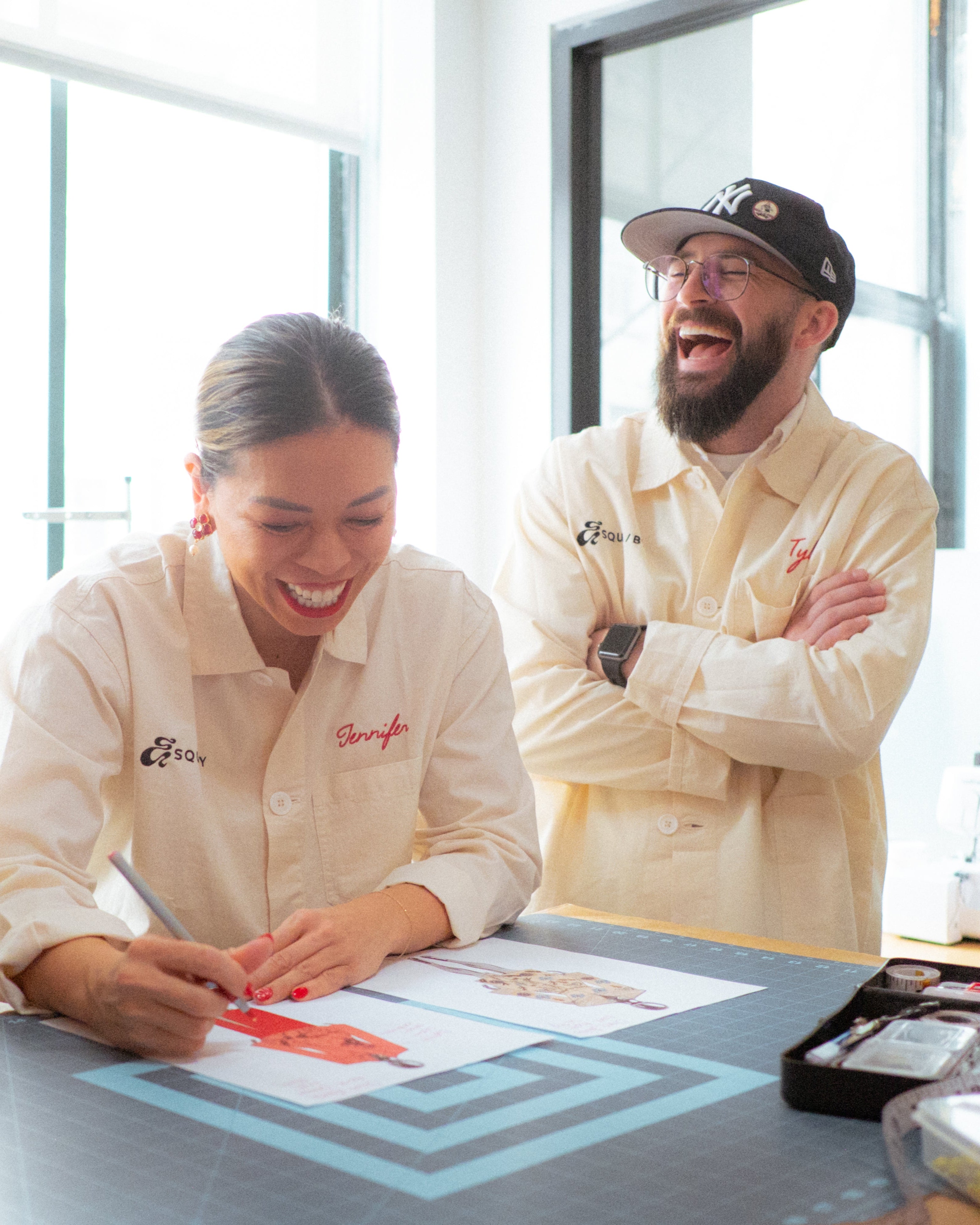 two people in branded lab coats gathered around a table with a digital display, smiling and engaged in a discussion.