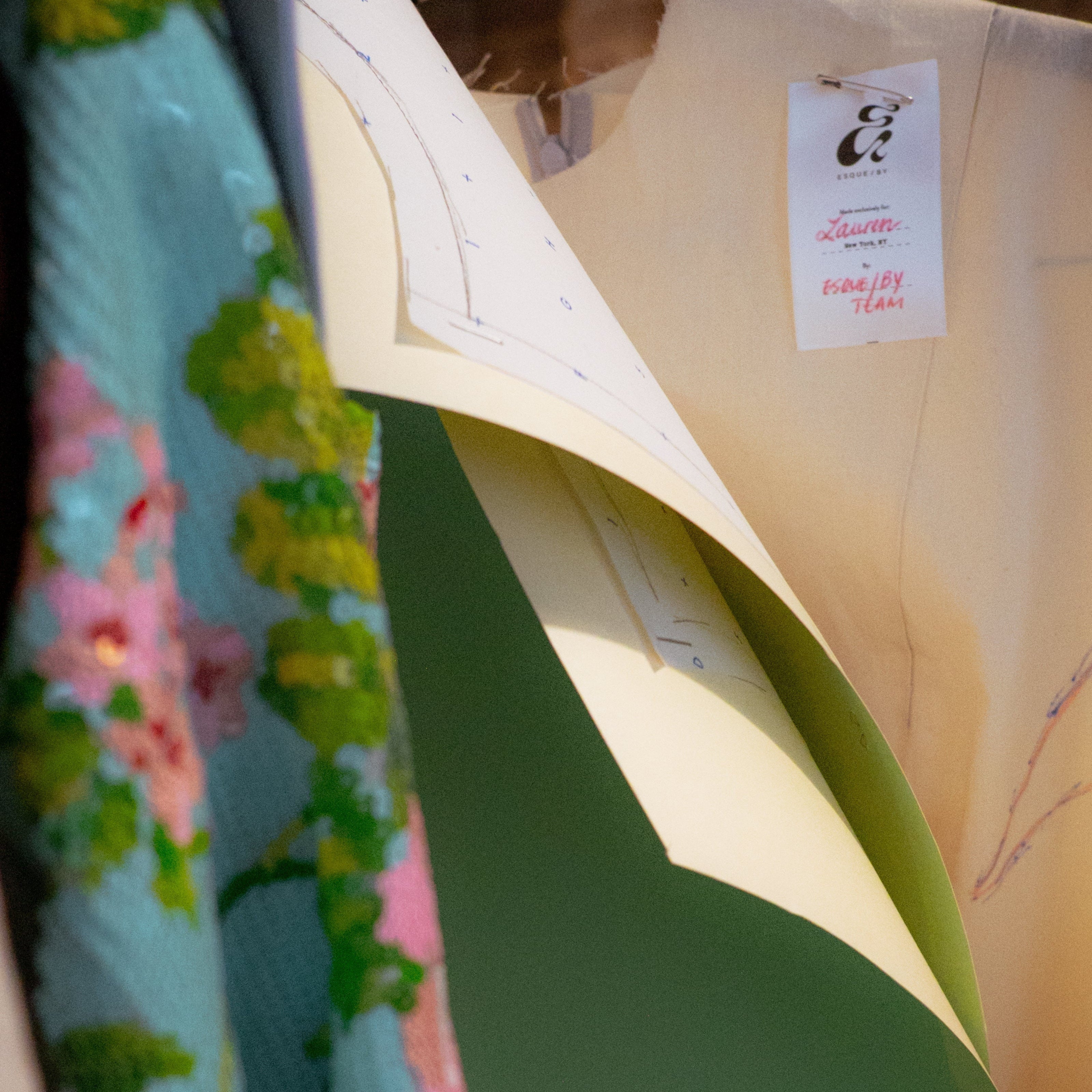 Close-up of a light-colored garment on a mannequin with a floral fabric in the background.