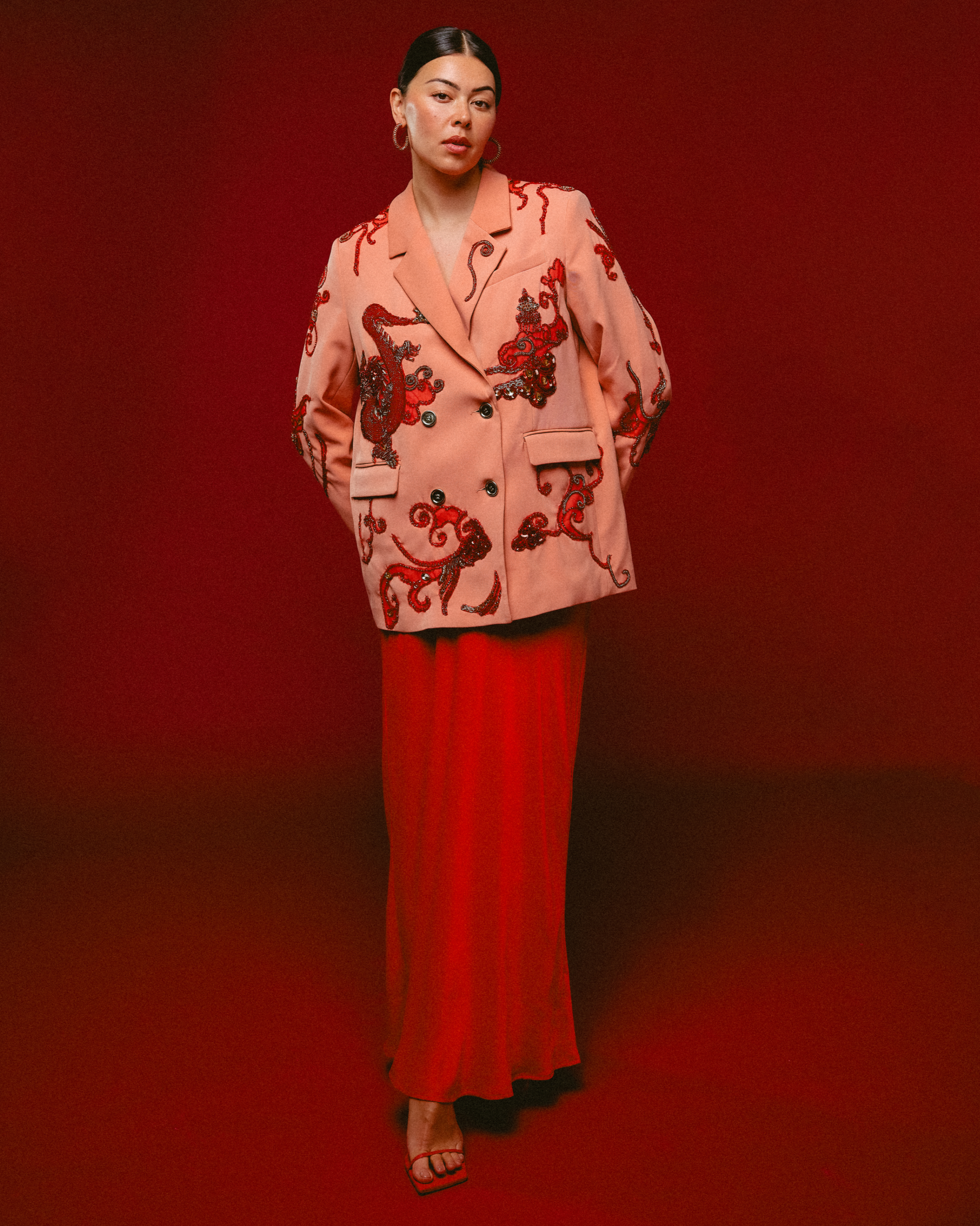Person wearing a pink embroidered blazer and red skirt against a red background