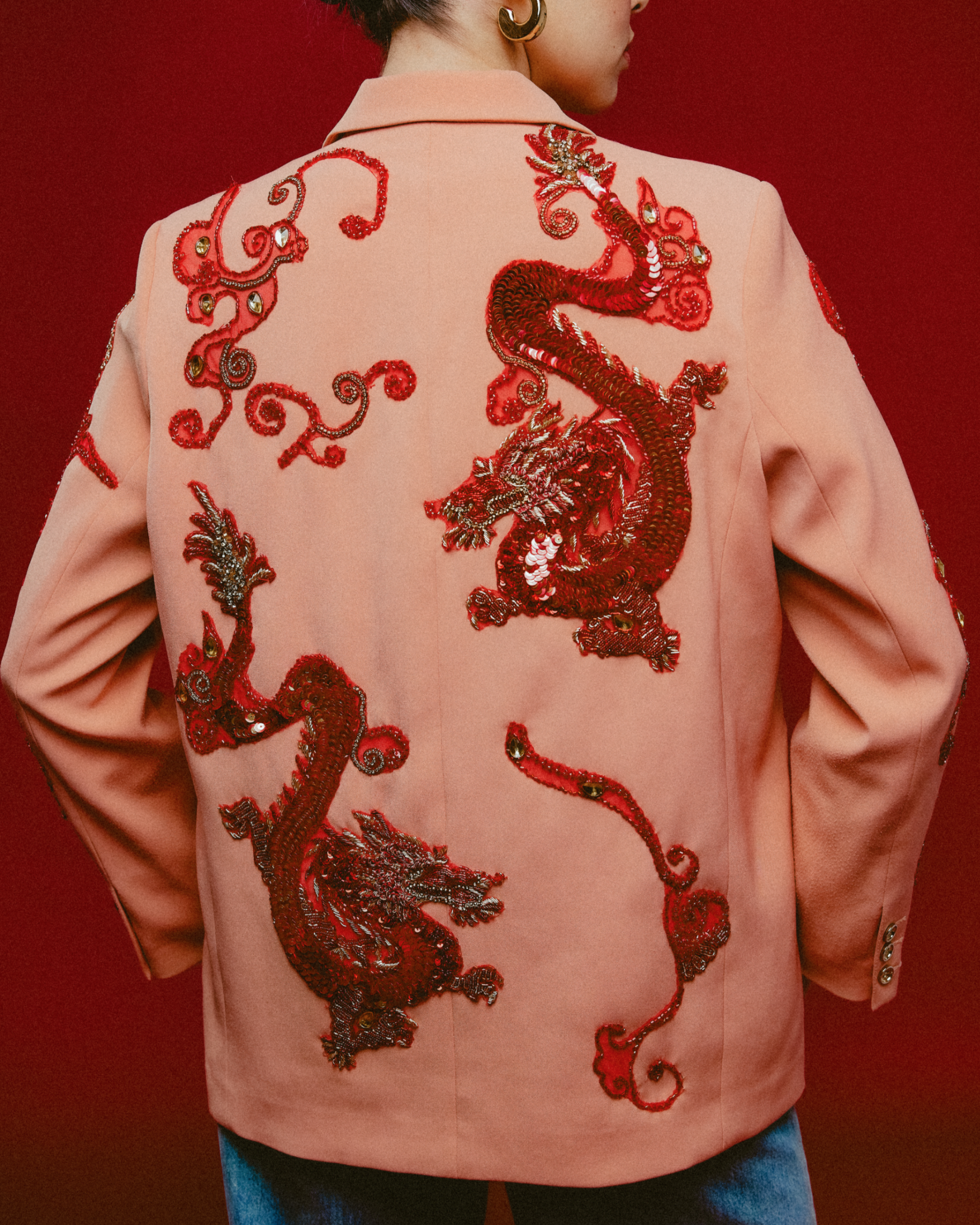 Person wearing a pink jacket with red dragon embroidery on a red background