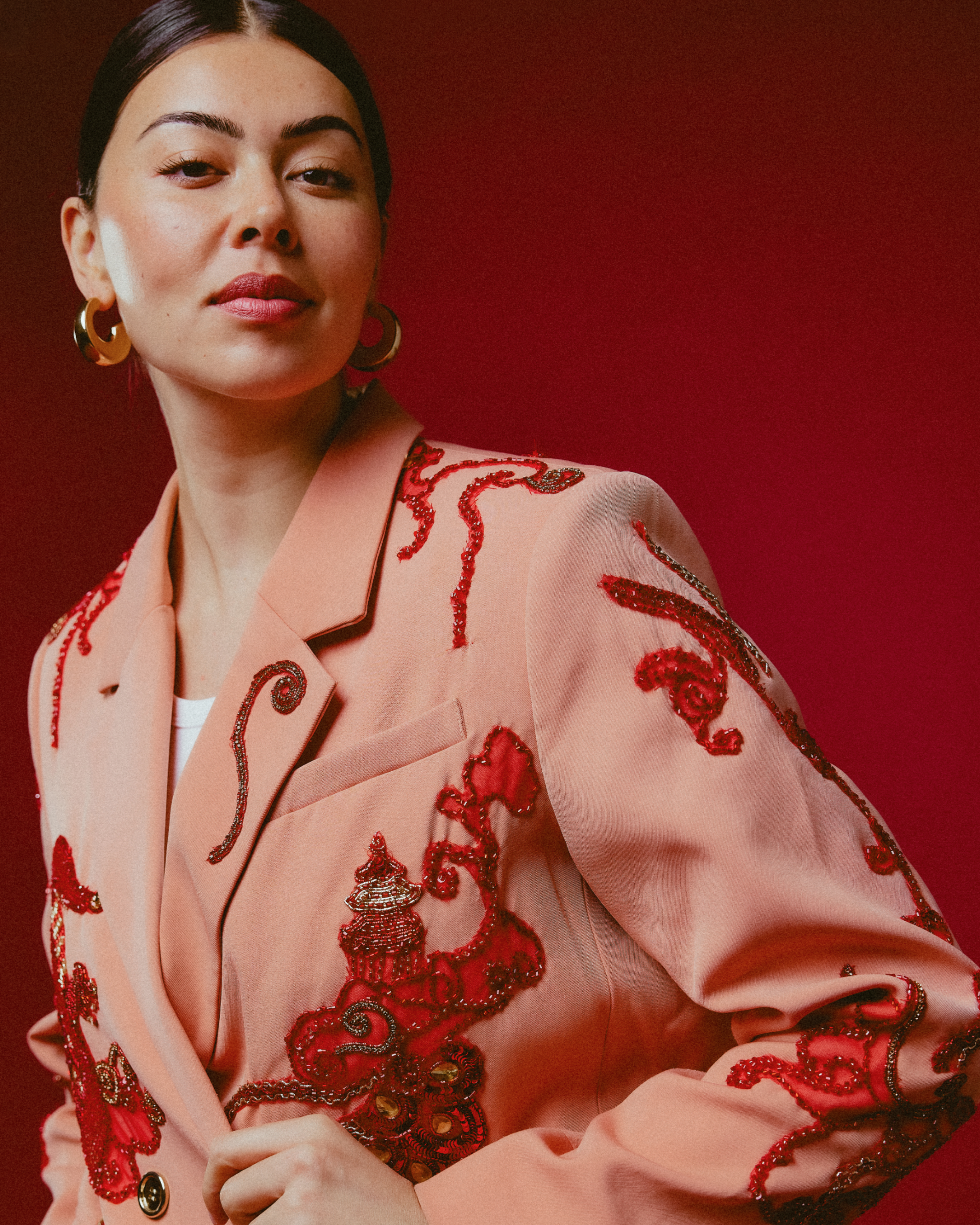 Woman wearing a pink outfit with red embroidery against a red background