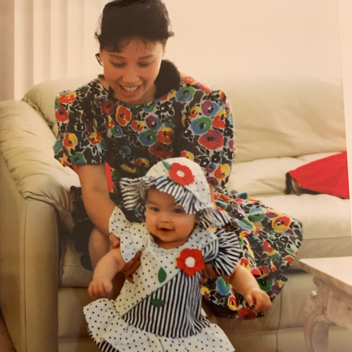 Woman and baby in floral and polka dot outfits standing in a living room.